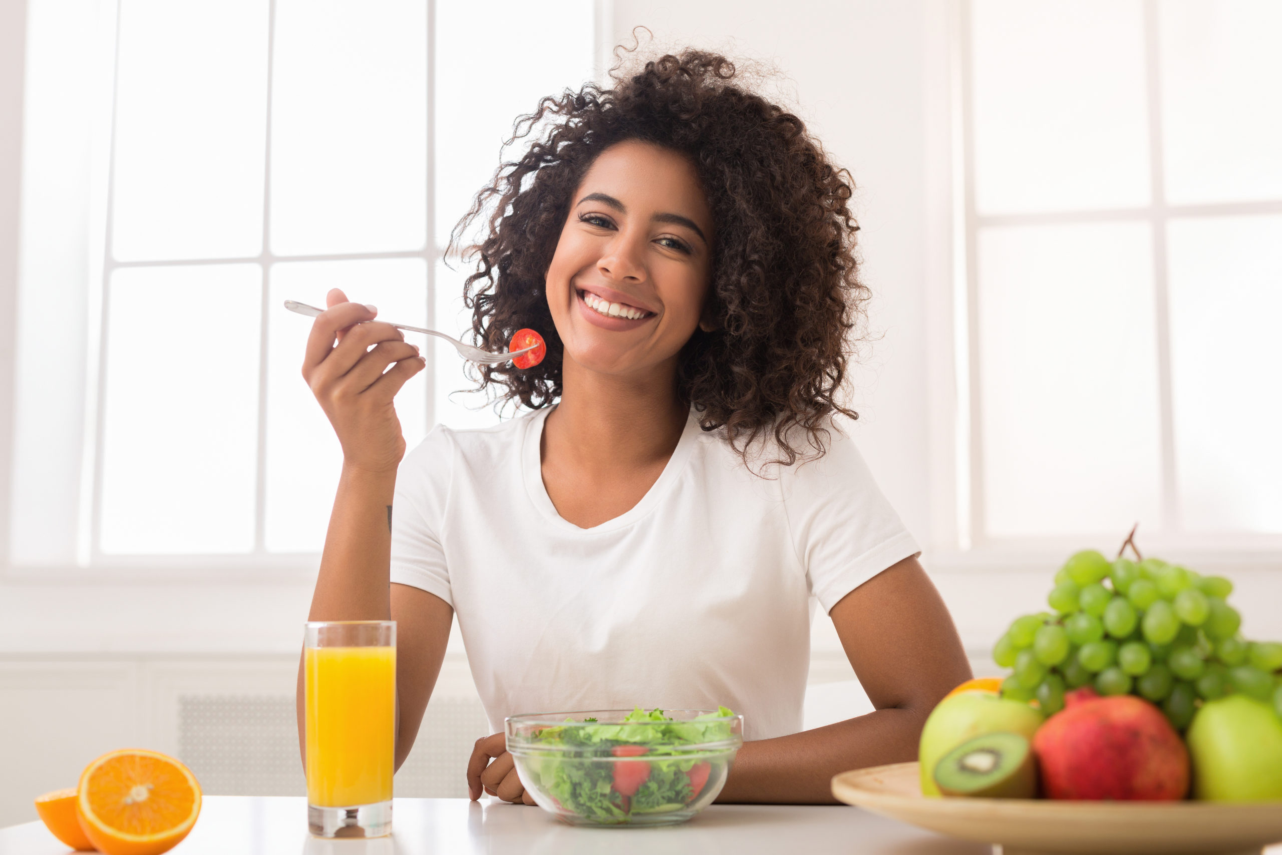 African-american woman eating vegetable salad and drinking fresh juice at home